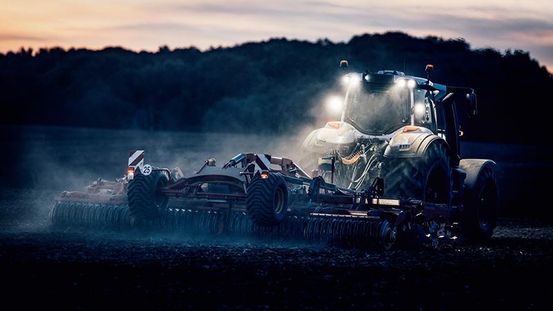 Máquina agrícola com implemento operando no fim do dia
